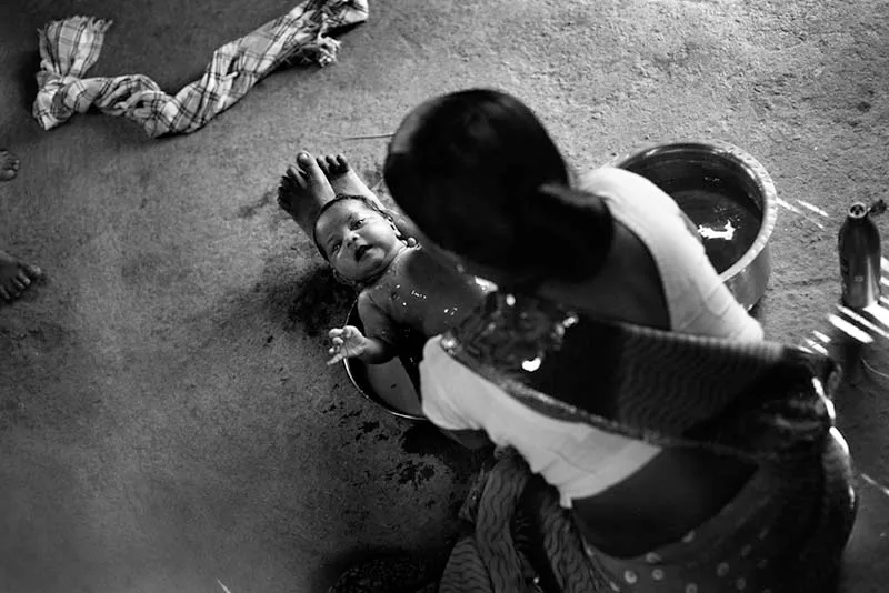 A mother giving a bath to her newborn child. Maharashtra, India.